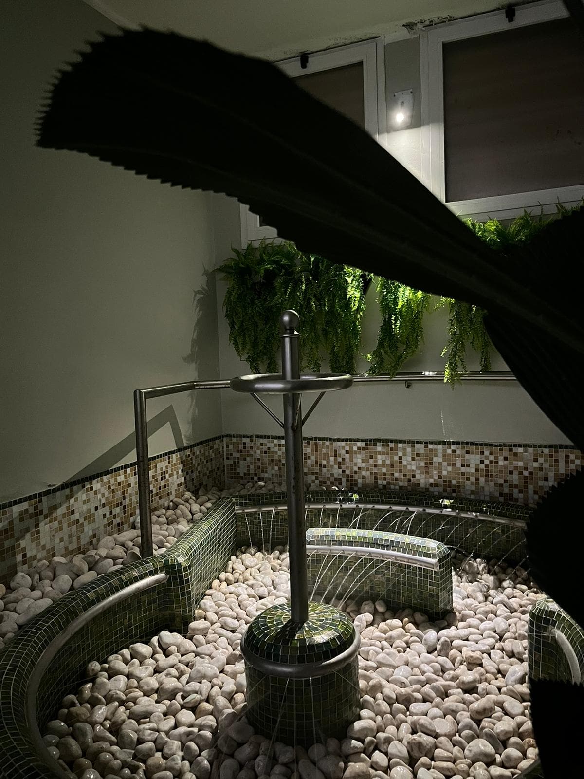 Percorso Kneipp con ciottoli bianchi, getti d'acqua e piante decorative