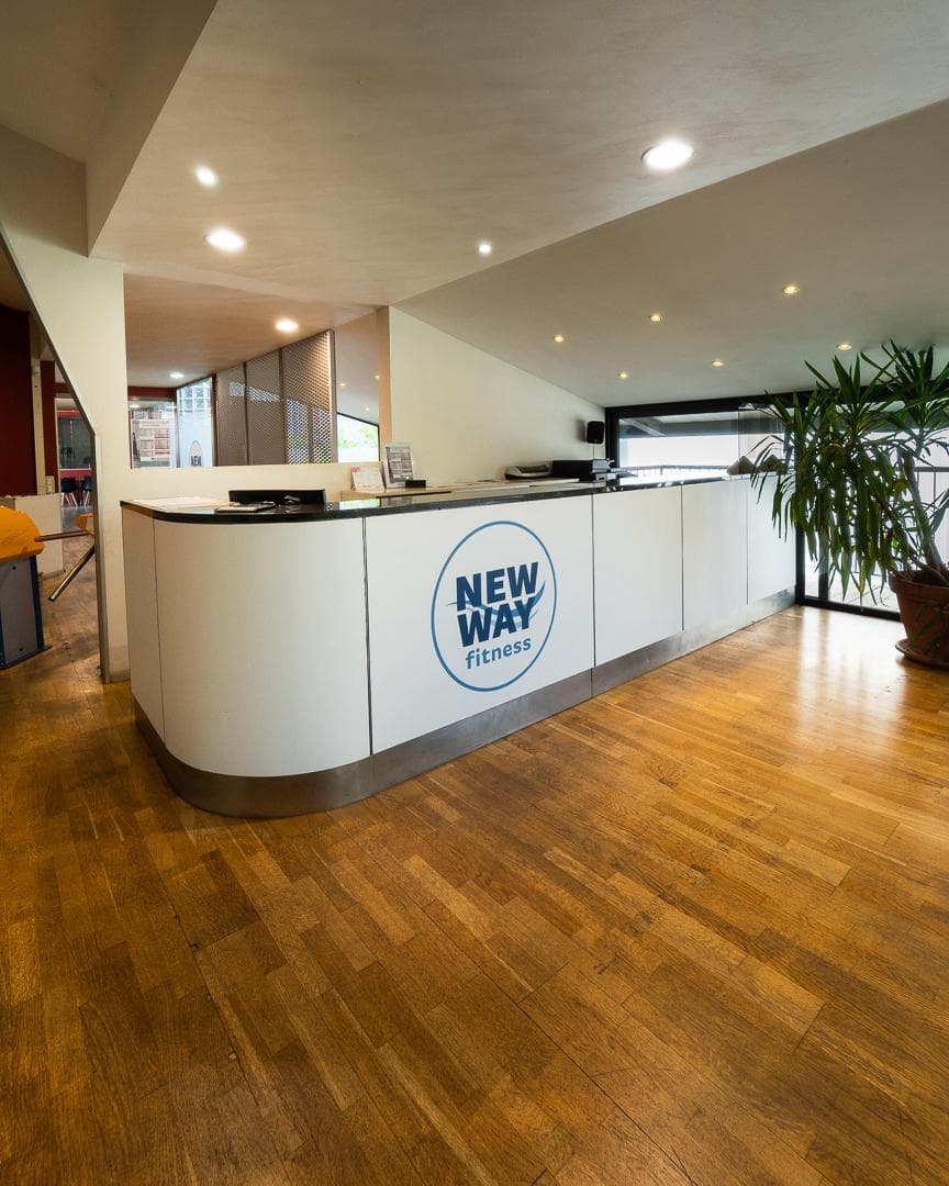 Reception New Way Fitness con bancone bianco, logo e pavimento in legno