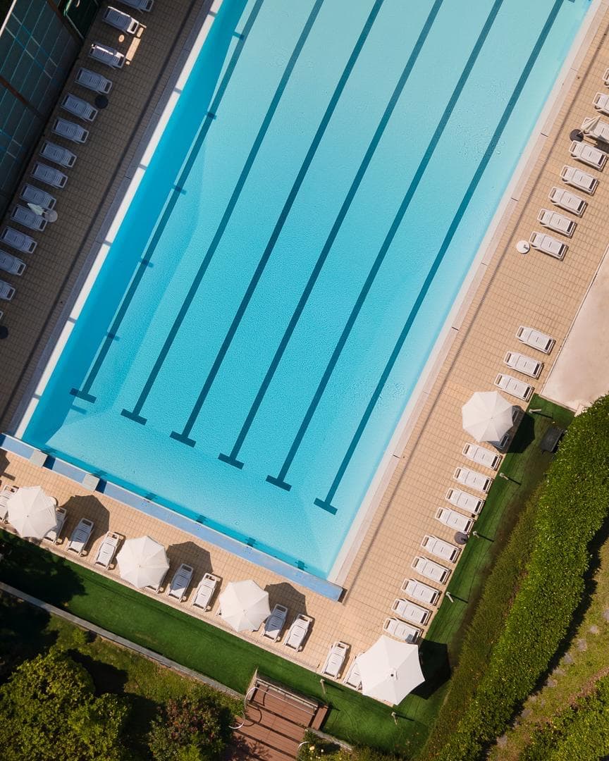 Piscina esterna da 25 metri vista dall'alto con corsie, lettini e ombrelloni
